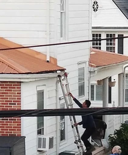 Person on ladder working on roof near power lines and white house