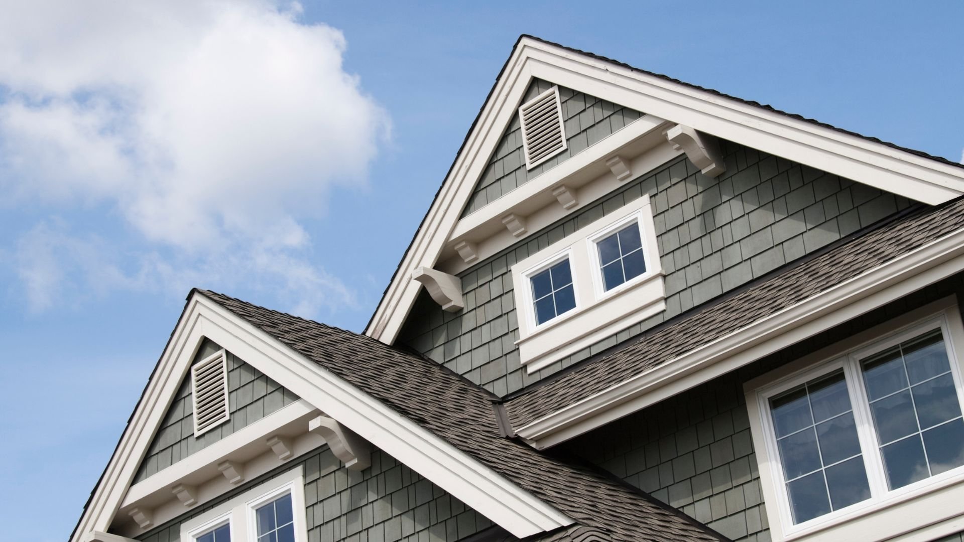 Gray shingled house with white trim and multiple windows under blue sky