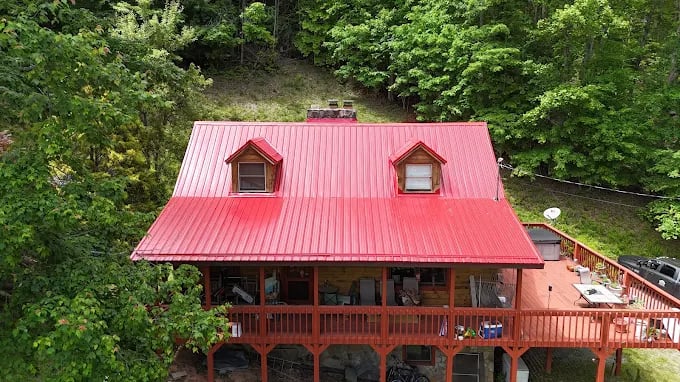 Red-roofed cabin with wooden deck nestled in lush green forest