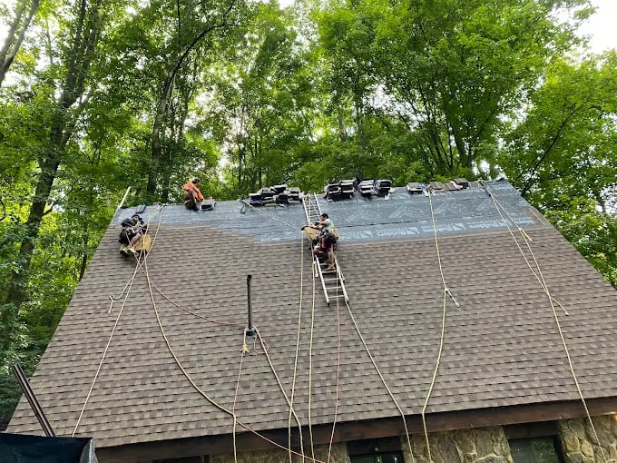 Roofers on safety ropes replacing shingles on a house in wooded area