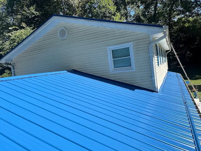 Bright blue metal roof on white vinyl-sided building with trees