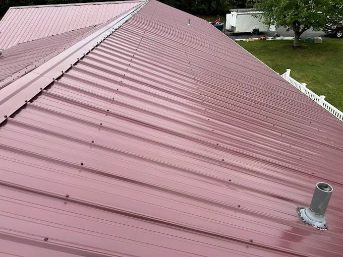 Pink metal roof with ribbed panels and white fence in background