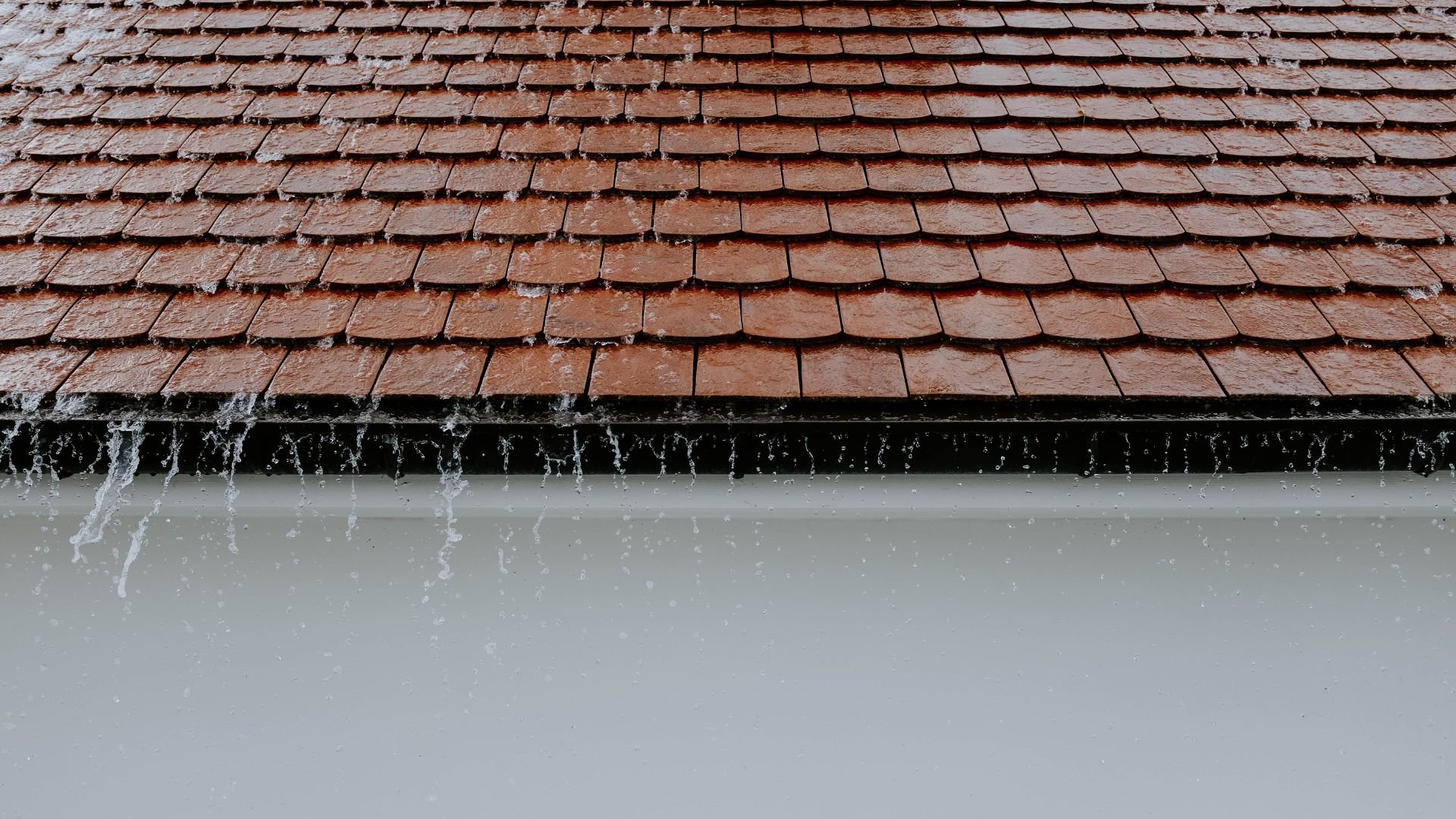 Wet wooden roof shingles with rainwater dripping down gutter edge