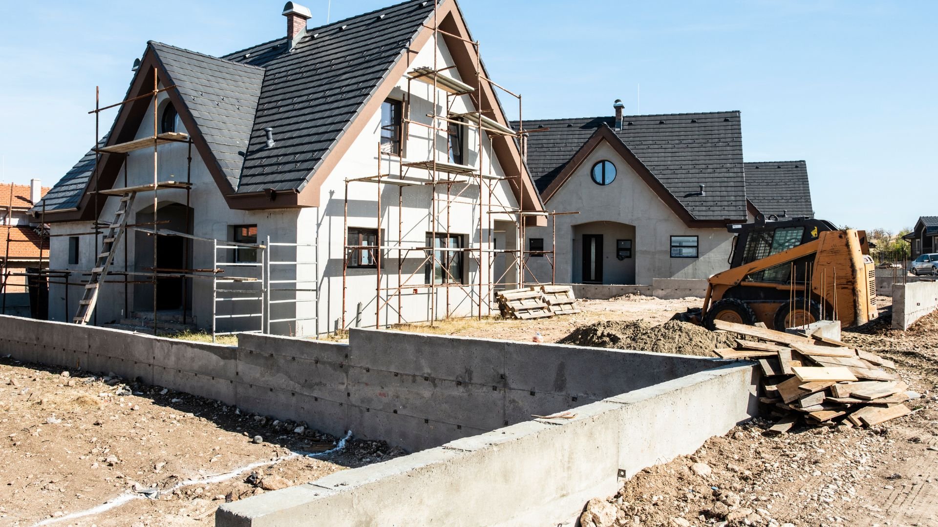 Houses under construction with scaffolding, concrete foundation, and construction equipment