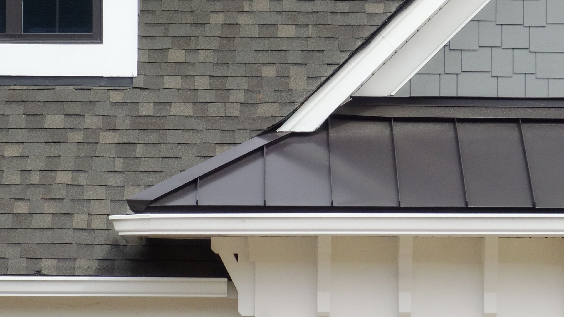 Close-up of house roof with metal and shingle sections in gray tones