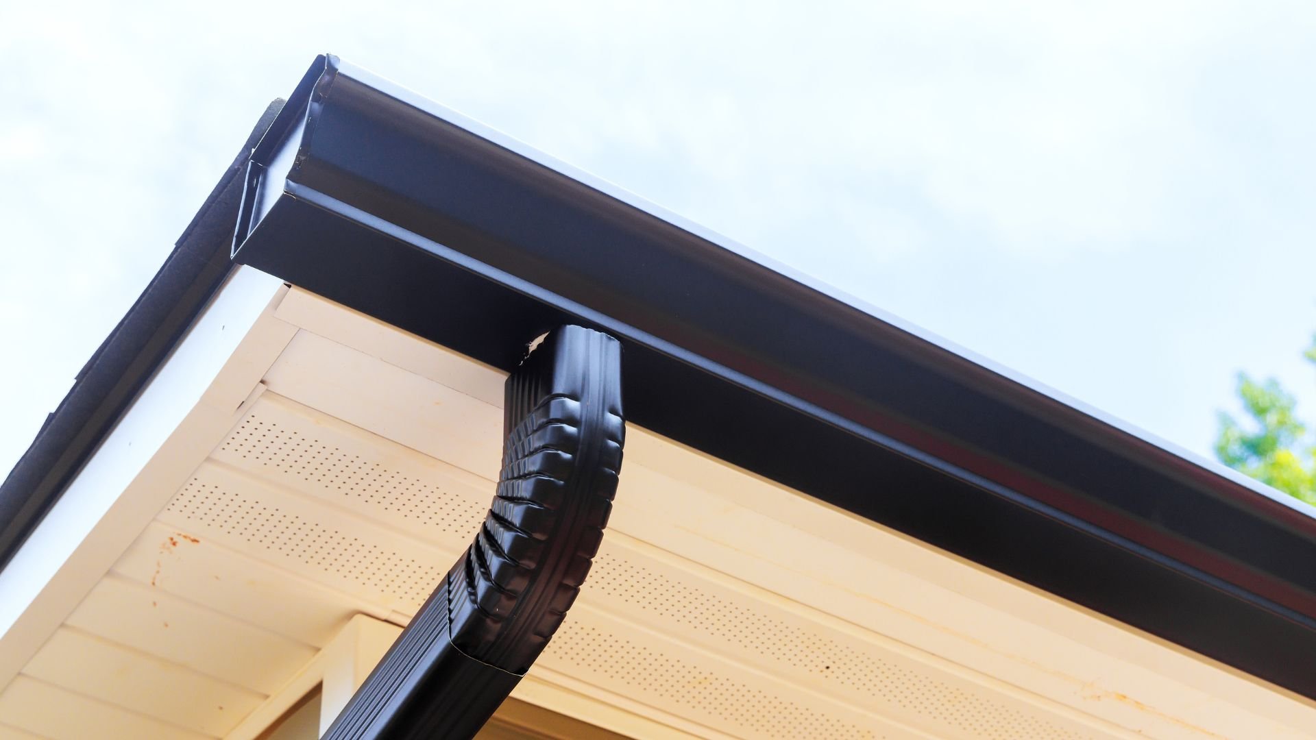 Black gutter and downspout attached to beige soffit of modern building