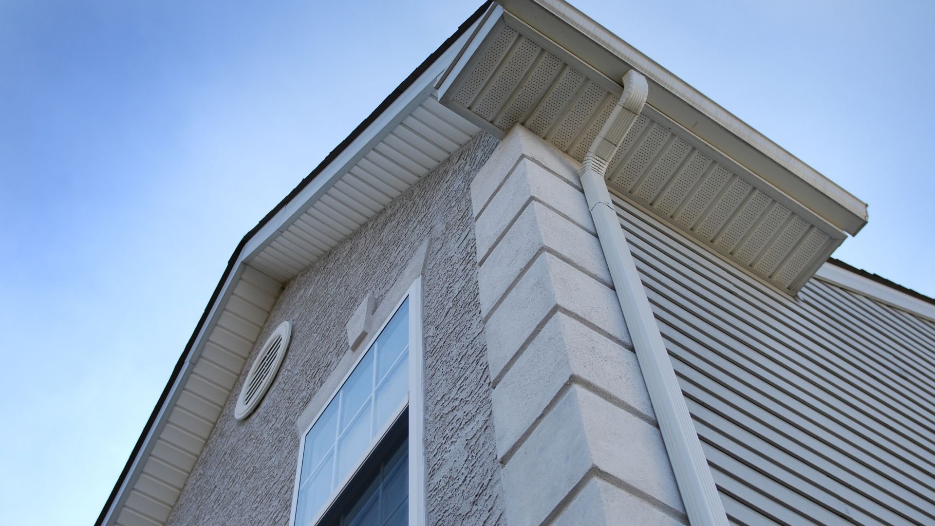 White house exterior corner with window and textured siding against blue sky