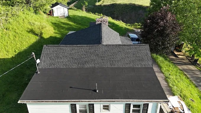 Aerial view of house roof with gray shingles and green surroundings