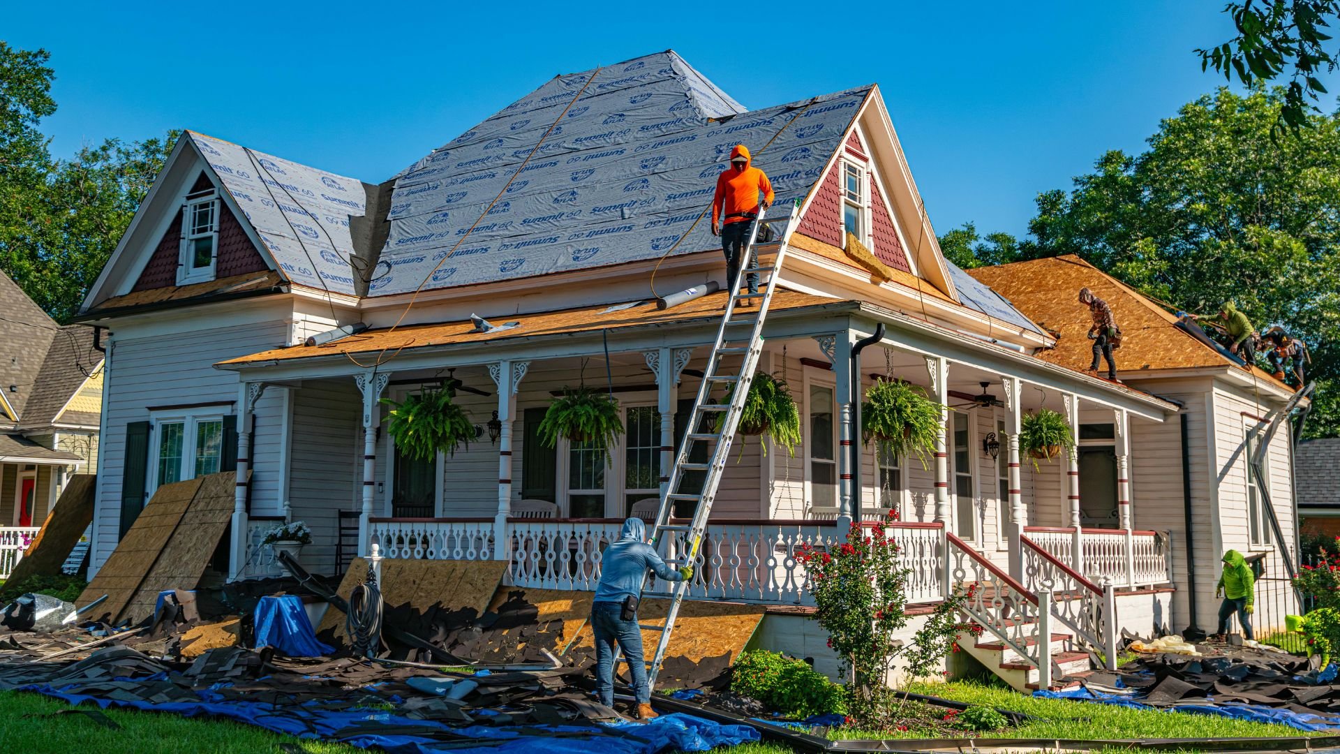 Workers replacing roof on Victorian-style house with blue sky background