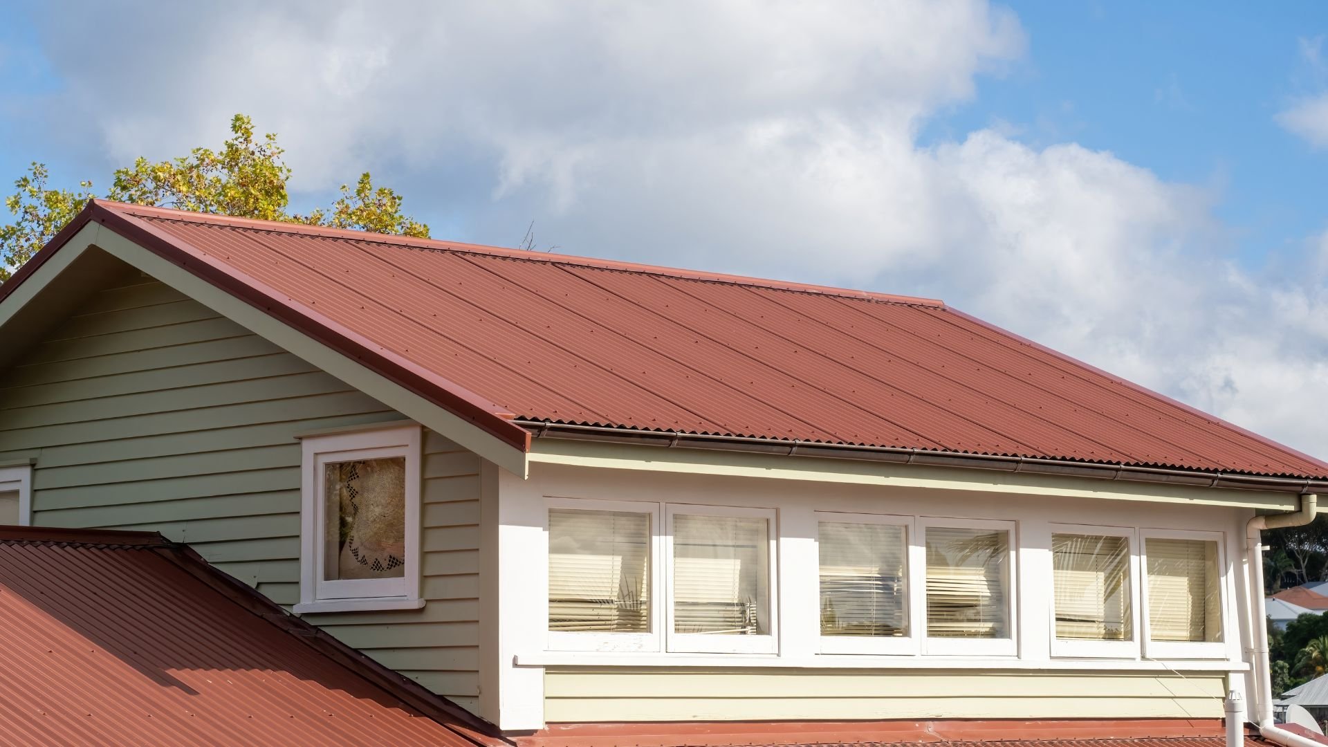 Red metal roof house with white windows and green siding on cloudy day