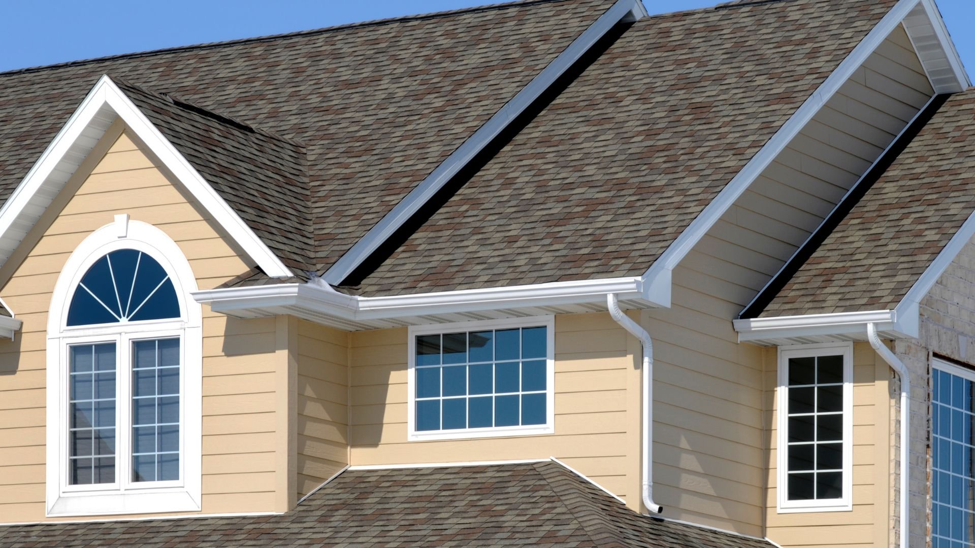 Yellow house with multiple windows and multi-toned brown shingle roof