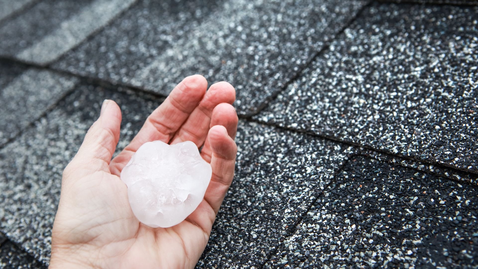 Large hailstone held in hand over textured gray surface